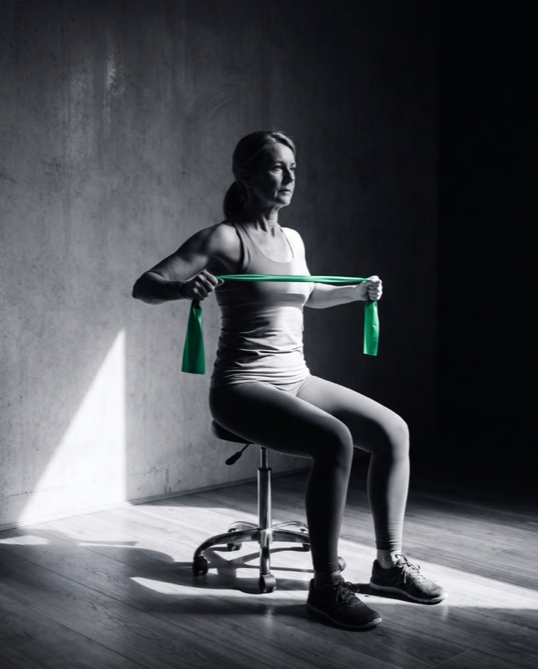 A woman performing a seated resistance band shoulder exercise