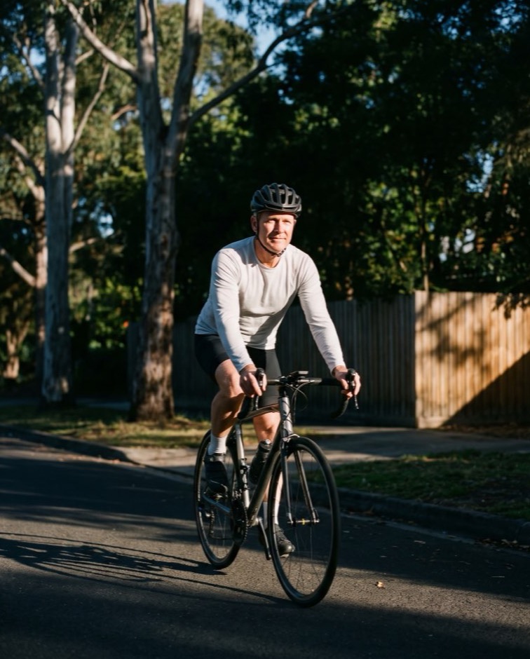 A man riding a bicycle along a suburban bike path in the morning